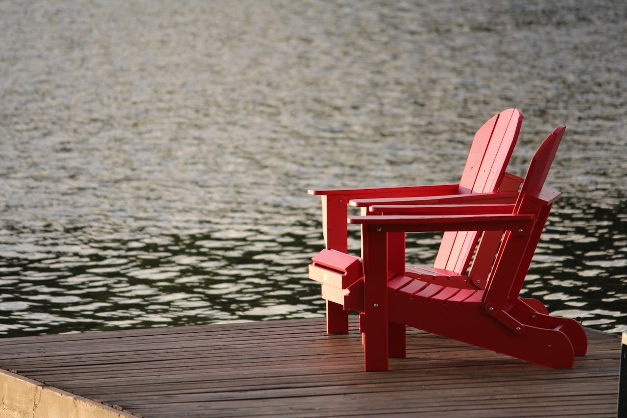 Services Two red Adirondack chairs on a wooden dock overlooking peaceful waters, ideal for relaxation.
